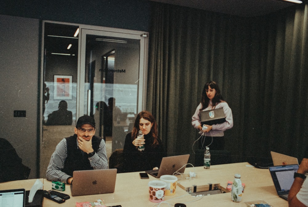 a group of people sitting around a table with laptops