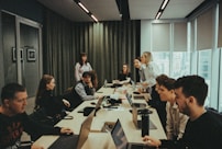 a group of people sitting around a table with laptops