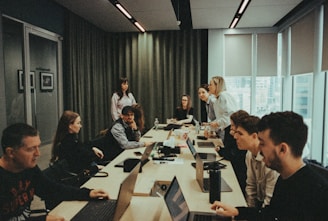 a group of people sitting around a table with laptops
