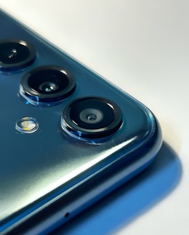 A close-up view of a smartphone's camera module featuring multiple lenses and a small LED flash. The metallic surface of the phone reflects light, giving it a sleek and modern appearance.