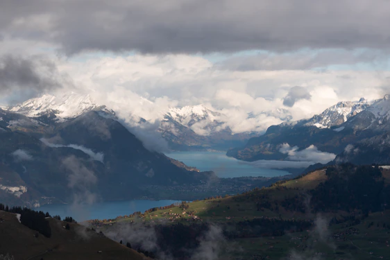 A breathtaking panoramic view of Saint Moritz's snowy mountains and crystal-clear lake under a bright blue sky.