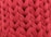 A close-up view of an intricate red knitted fabric with a thick, chunky texture. The woven pattern displays a series of large, interlocking loops creating a visually rich surface.