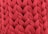 A close-up view of an intricate red knitted fabric with a thick, chunky texture. The woven pattern displays a series of large, interlocking loops creating a visually rich surface.