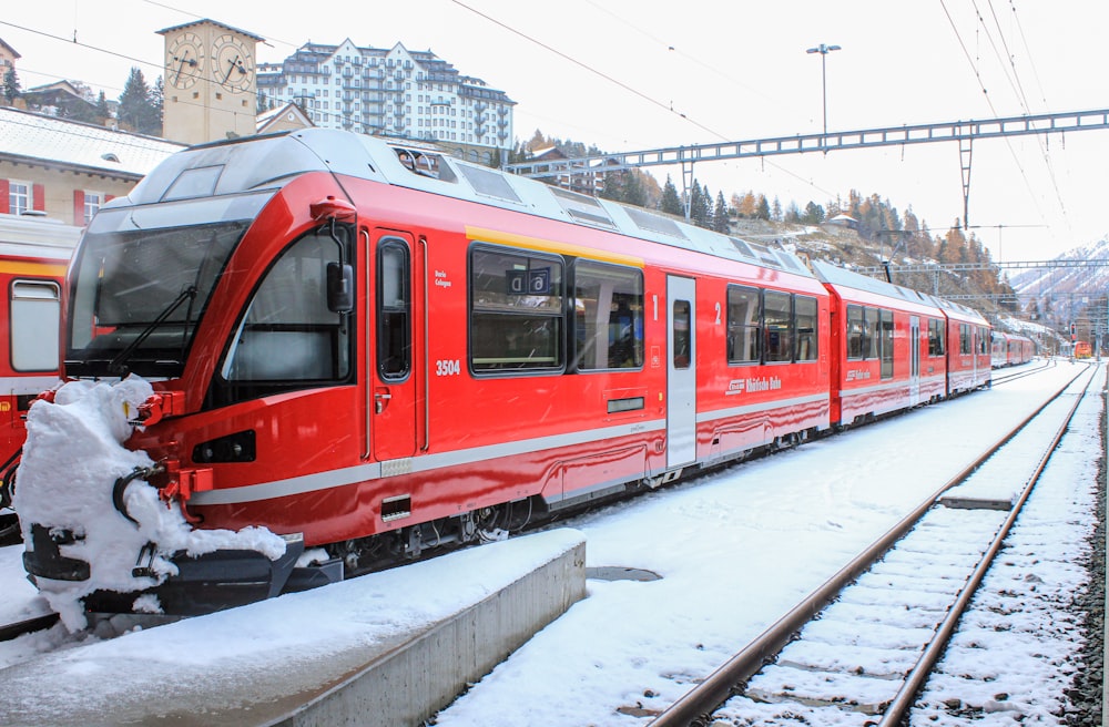 a red train traveling down train tracks next to a snow covered platform