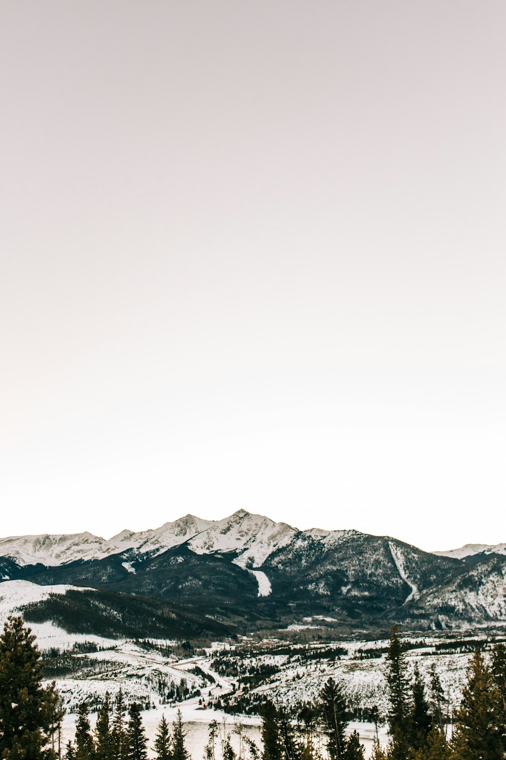 a view of a snowy mountain range with trees in the foreground