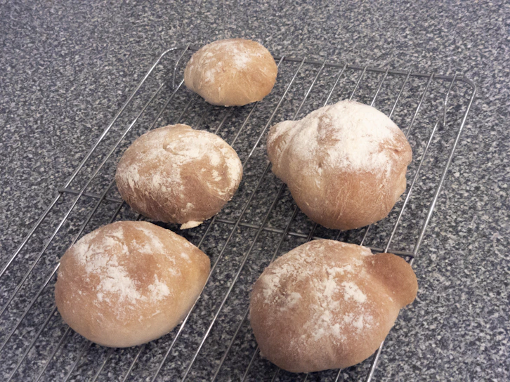 Close-up of freshly baked golden bolillos cooling on a wooden rack.