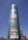 A tall cylindrical glass building displaying colorful large-font words like Drama, History, Skill, Art, Faith, Style, Passion, and Football. Free entry and open daily signs are visible at the bottom. Streetlights and a few other buildings are in the vicinity under a clear blue sky.