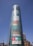 A tall cylindrical glass building displaying colorful large-font words like Drama, History, Skill, Art, Faith, Style, Passion, and Football. Free entry and open daily signs are visible at the bottom. Streetlights and a few other buildings are in the vicinity under a clear blue sky.