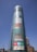 A tall cylindrical glass building displaying colorful large-font words like Drama, History, Skill, Art, Faith, Style, Passion, and Football. Free entry and open daily signs are visible at the bottom. Streetlights and a few other buildings are in the vicinity under a clear blue sky.