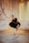 A ballet dancer is posed in a graceful position within an elegantly aged room with textured walls and soft lighting. She is dressed in a black lace ballet costume with a classic tutu, and wears pointe shoes. The ambiance is warm and vintage, with an arched window allowing a gentle glow into the room, highlighting the intricate architectural details of the walls.