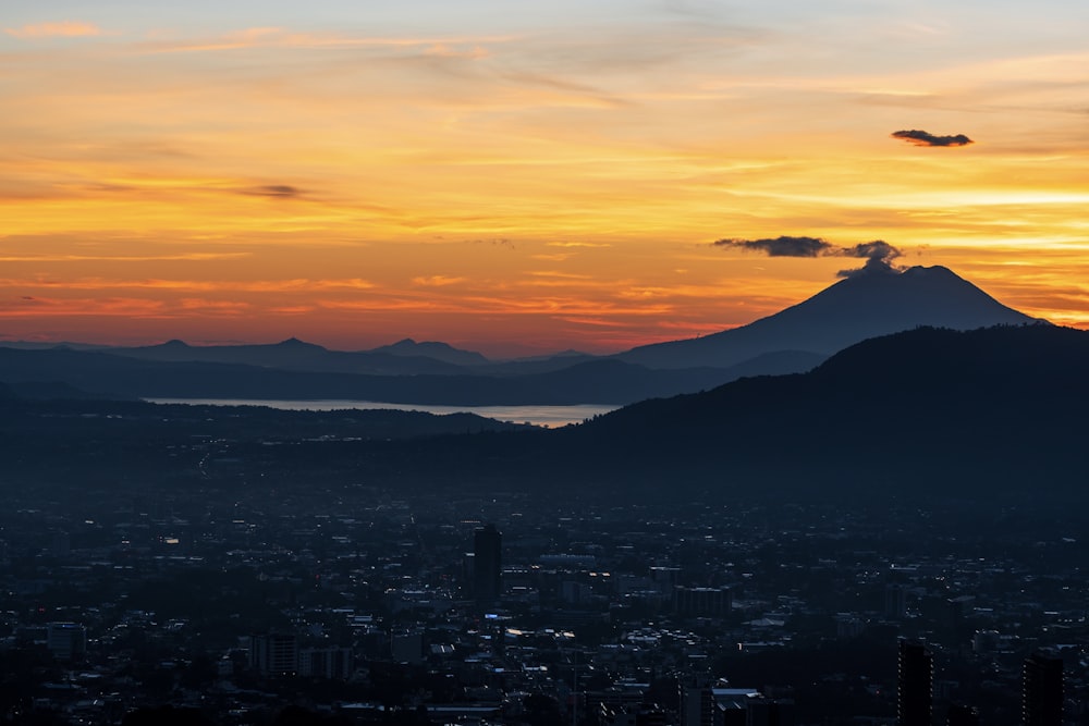 a sunset view of a city with a mountain in the background