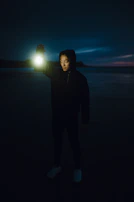 Close-up of a hand holding a glowing lantern in a dark forest, symbolizing guidance.