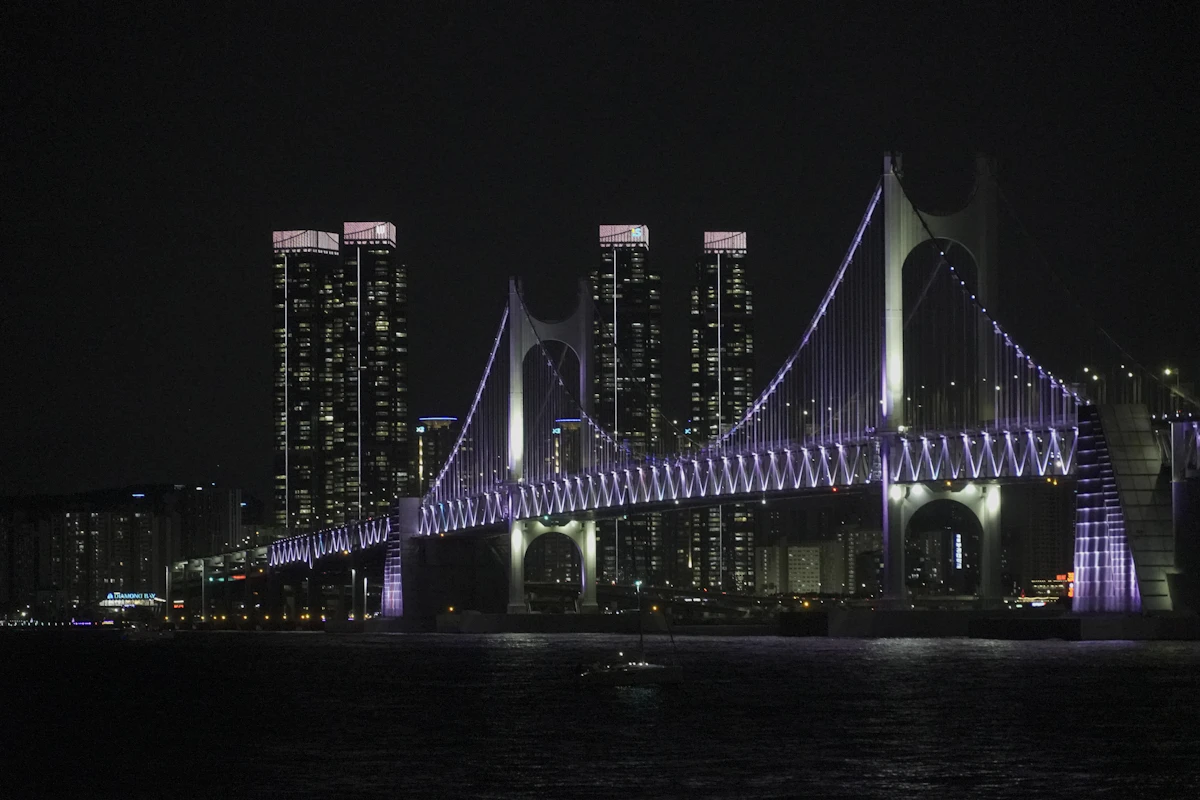 Gwangan Bridge lit in purple at night, high-rise apartments behind it