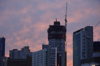 A modern city skyline at sunset with cranes and new buildings under construction, symbolizing growth and opportunity.