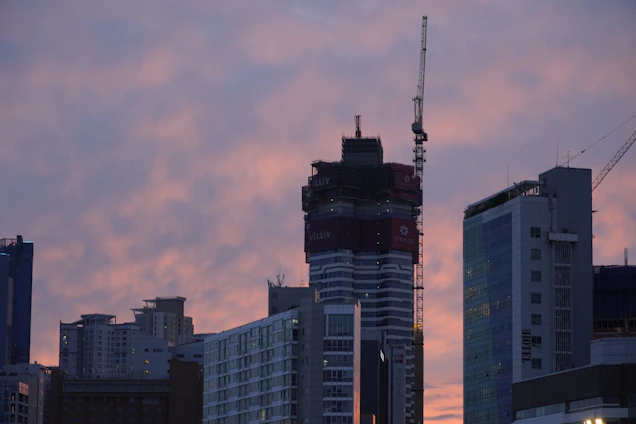 A modern city skyline at sunset with cranes and new buildings under construction, symbolizing growth and opportunity.
