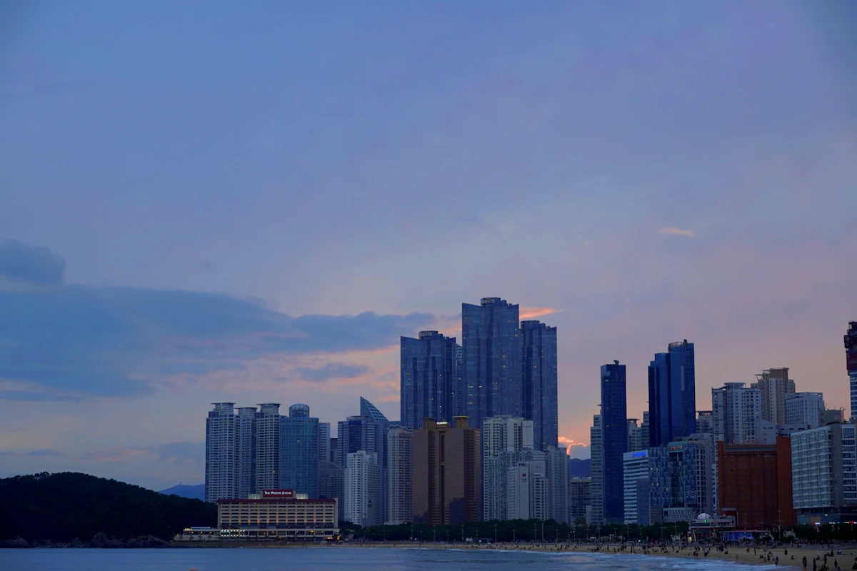 Haeundae beachfront high-rises seen across the water at dusk, a hill on the left