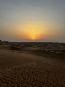 A serene desert landscape with the sun setting behind the dunes near the Siwa Oasis.