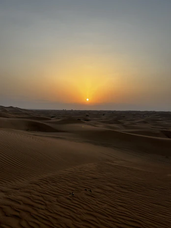 A serene landscape of the Sahara desert at sunset with warm golden hues.