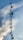 A tall communication tower with multiple satellite dishes and antennas is silhouetted against a cloudy sky. The structure is held in place by numerous cables, and the sky is predominantly blue with patches of white clouds.