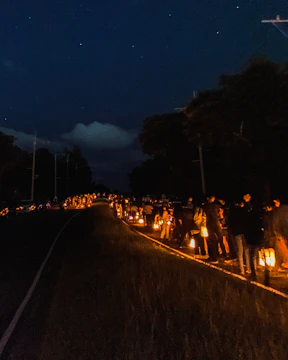 Group of walkers holding candles marching along a desert trail at dusk framed by mountains.
