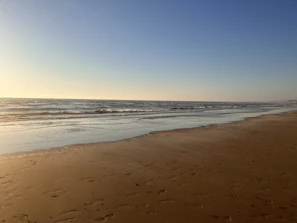 A serene beach scene at dawn with soft waves and footprints in the sand