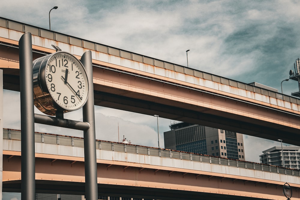 a clock on a pole in front of a bridge