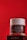 A jar of Age Revive night cream from Oriflame is placed against a bold red background. The jar is transparent with a white lid, featuring text detailing its benefits and ingredients. It rests on a dark box with brand titling.