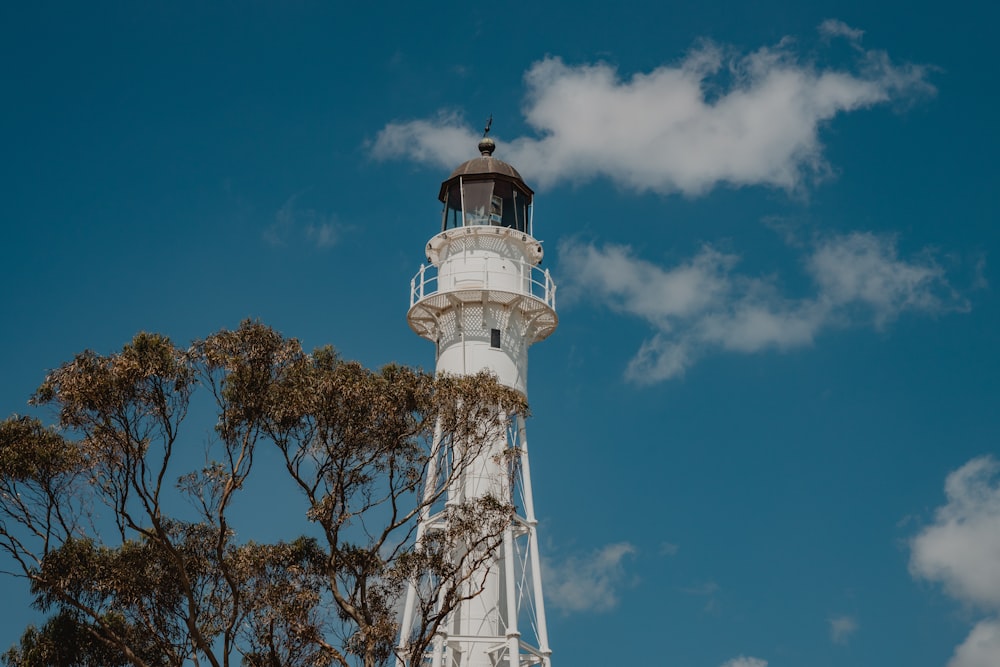 a white light house surrounded by trees under a blue sky