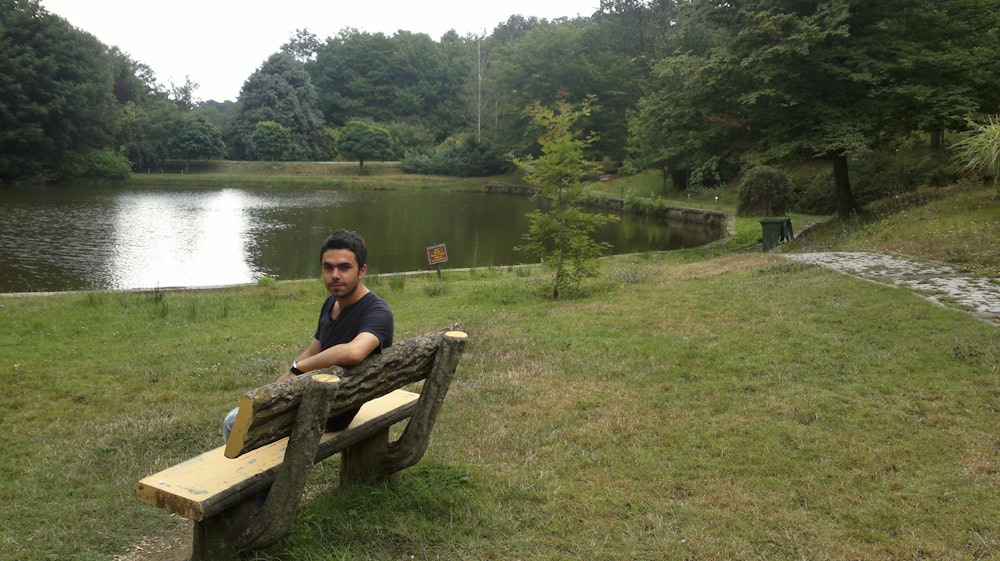 a man sitting on a wooden bench next to a lake