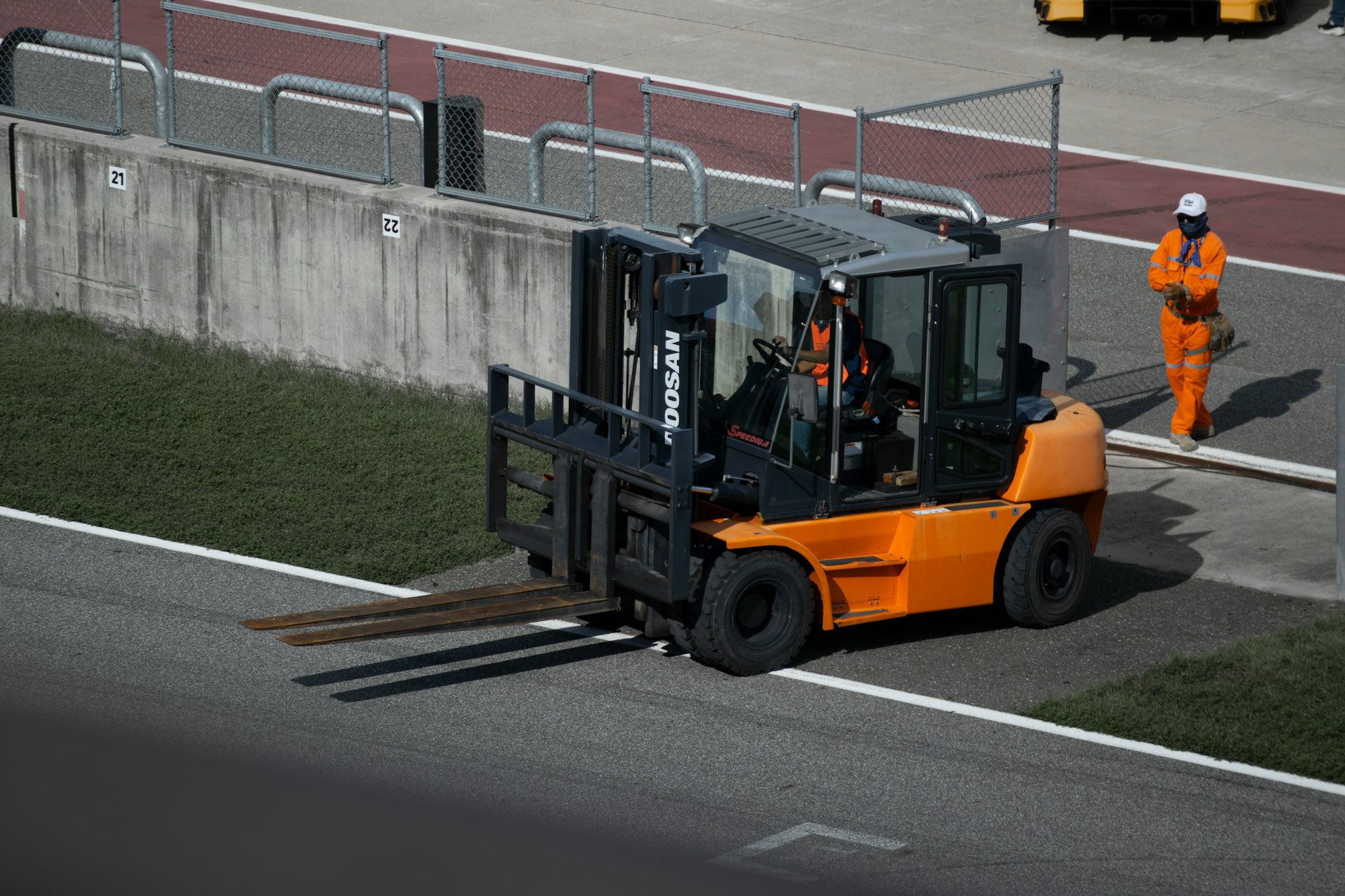 a forklift driving down a road next to a fence