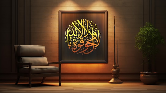 A cozy interior scene featuring a wooden wall adorned with an ornate framed piece of Arabic calligraphy. The calligraphy is illuminated with warm lighting, emphasizing its yellow and golden hues. Beside the artwork is an armchair with plush cushions, adding to the comfortable ambiance. A large, leafy plant in a pot and a tall, slender decorative element are positioned to the right, enhancing the tranquil and elegant atmosphere.