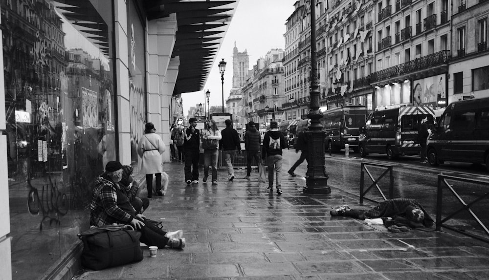 a black and white photo of people sitting on the sidewalk