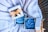 Gift boxes with blue rose-shaped candles are placed on a textured, fluffy blanket. Each box is adorned with a gold ribbon and contains a carefully crafted candle resembling a rose.