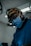 A person wearing surgical attire and a face mask, utilizing a magnifying headlamp in a medical setting. The environment appears sterile with dim lighting, highlighting the focus on precision and skill. The individual is deeply concentrated on their task.