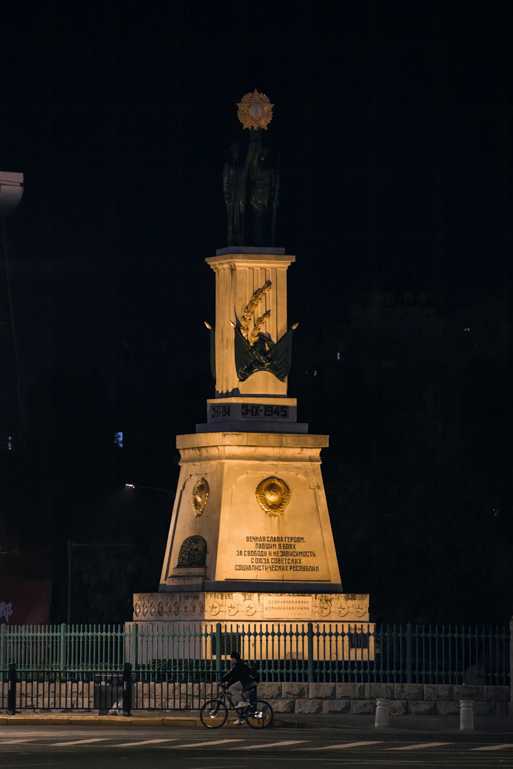 a man riding a bike past a monument at night