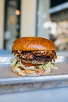 Stack of smashed burgers with fresh lettuce, tomato, and pickles on a vibrant blue plate.