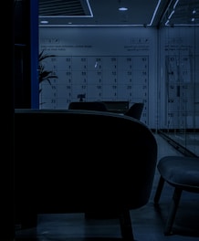 A dimly lit locker room with a modern design, featuring numbered lockers from 01 to 36. The numbers are clearly visible, and a motivational phrase on the wall reads 'Don't Keep Your Potential Locked Inside: Lock Up Your Purse!'. The seating area in the foreground consists of contemporary chairs, and there is a plant partially visible on the left side.