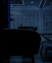 A dimly lit locker room with a modern design, featuring numbered lockers from 01 to 36. The numbers are clearly visible, and a motivational phrase on the wall reads 'Don't Keep Your Potential Locked Inside: Lock Up Your Purse!'. The seating area in the foreground consists of contemporary chairs, and there is a plant partially visible on the left side.