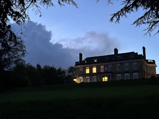 A twilight view of the old manor estate illuminated softly against a dark forest backdrop.