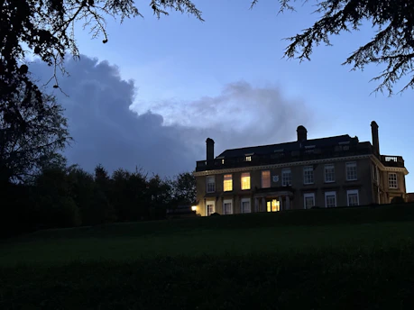 A twilight view of the old manor estate illuminated softly against a dark forest backdrop.