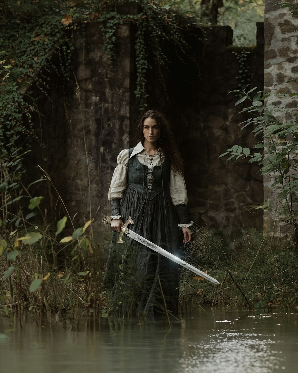 a woman in a dress holding a sword by a body of water