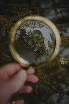 A close-up of hands holding a magnifying glass over an old, weathered family tree record.