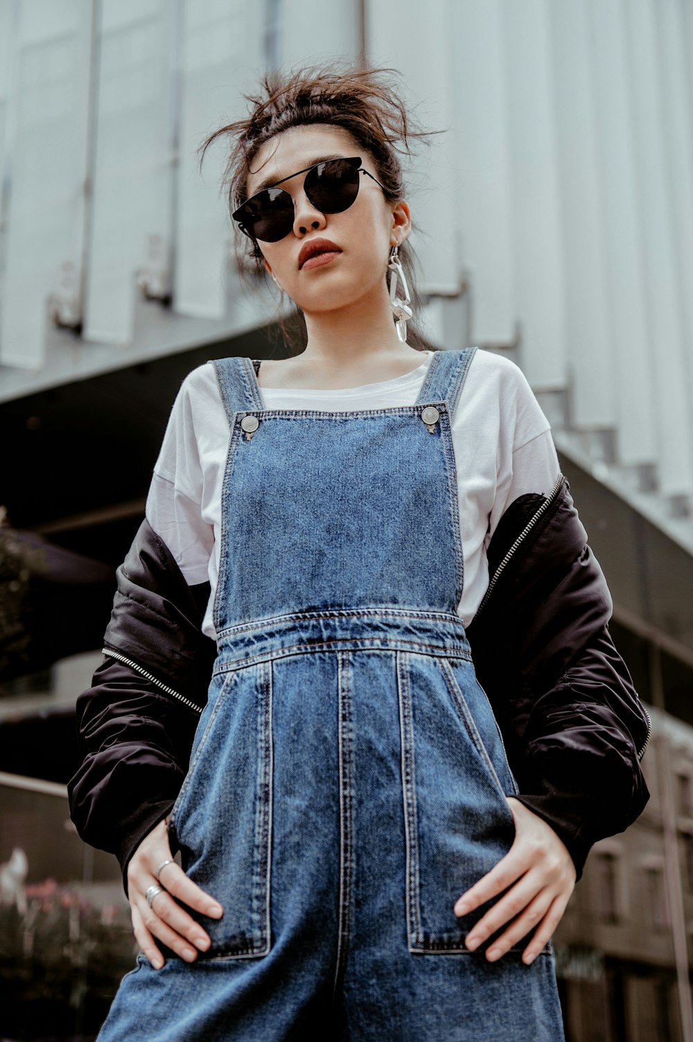 a woman in overalls and sunglasses standing in front of a building