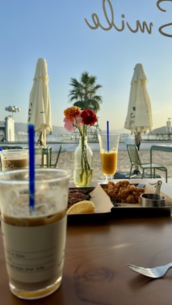 A cozy brunch table set outdoors with fresh pastries, smoothies, and sunlight filtering through trees.