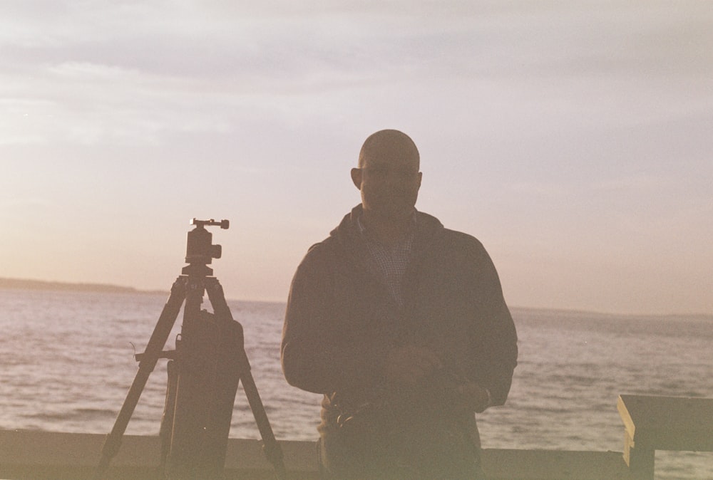 a man standing in front of a camera next to a body of water