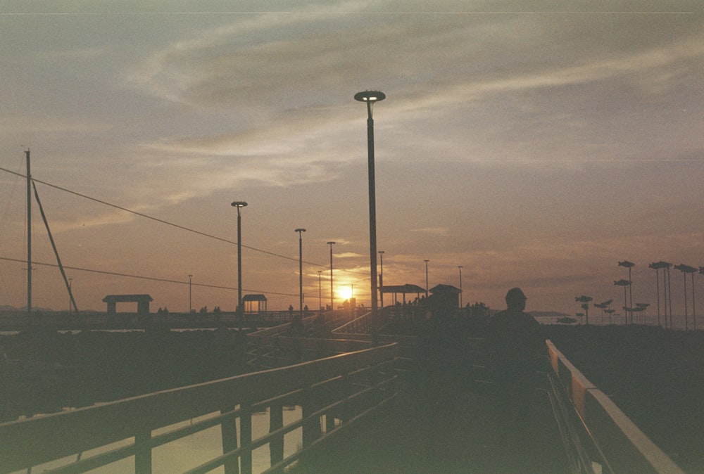 the sun is setting over a pier with lights