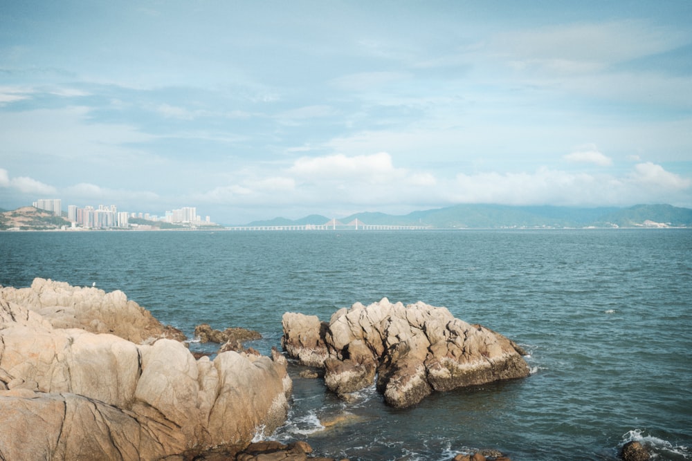 a body of water with rocks in the foreground and a city in the background