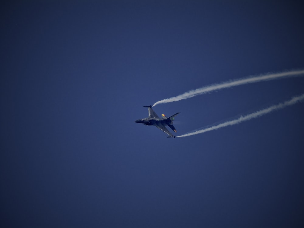 a jet flying through a blue sky leaving a trail of smoke behind it