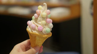 Close-up of a hand holding a swirled soft serve cone with bright pink and lime green colors against a retro pastel backdrop.