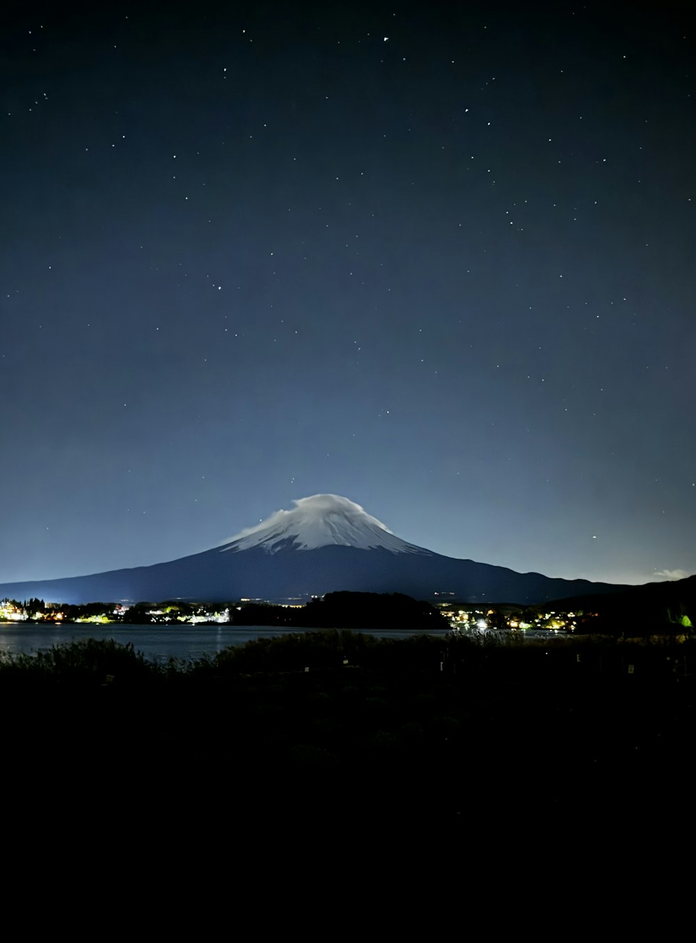 a night view of a mountain with a lake in the foreground